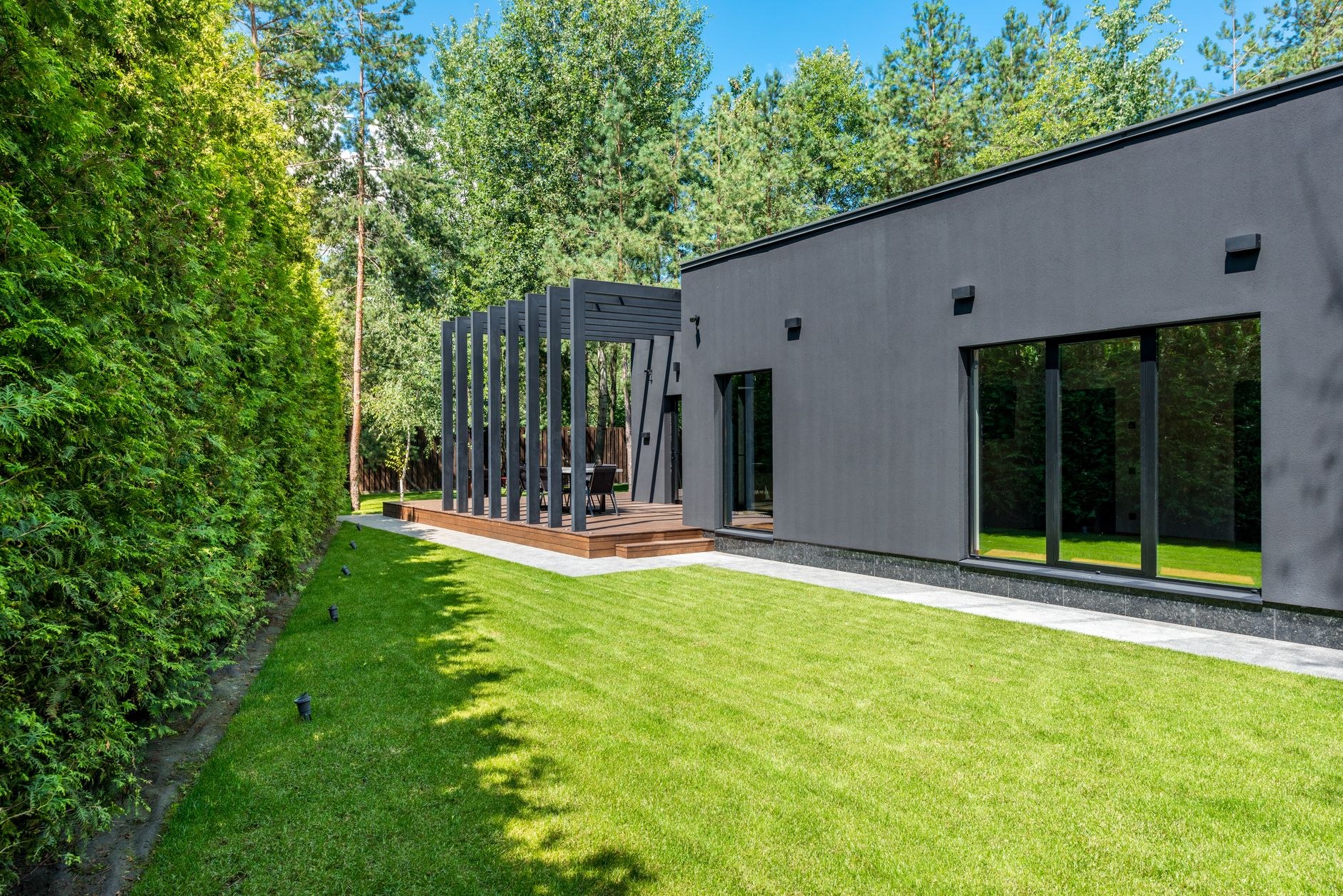 A tall, densely clipped hedge running the length of a modern home's garden boundary